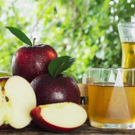 Fresh red apples and apple cider vinegar displayed in glass containers on rustic wooden surface.